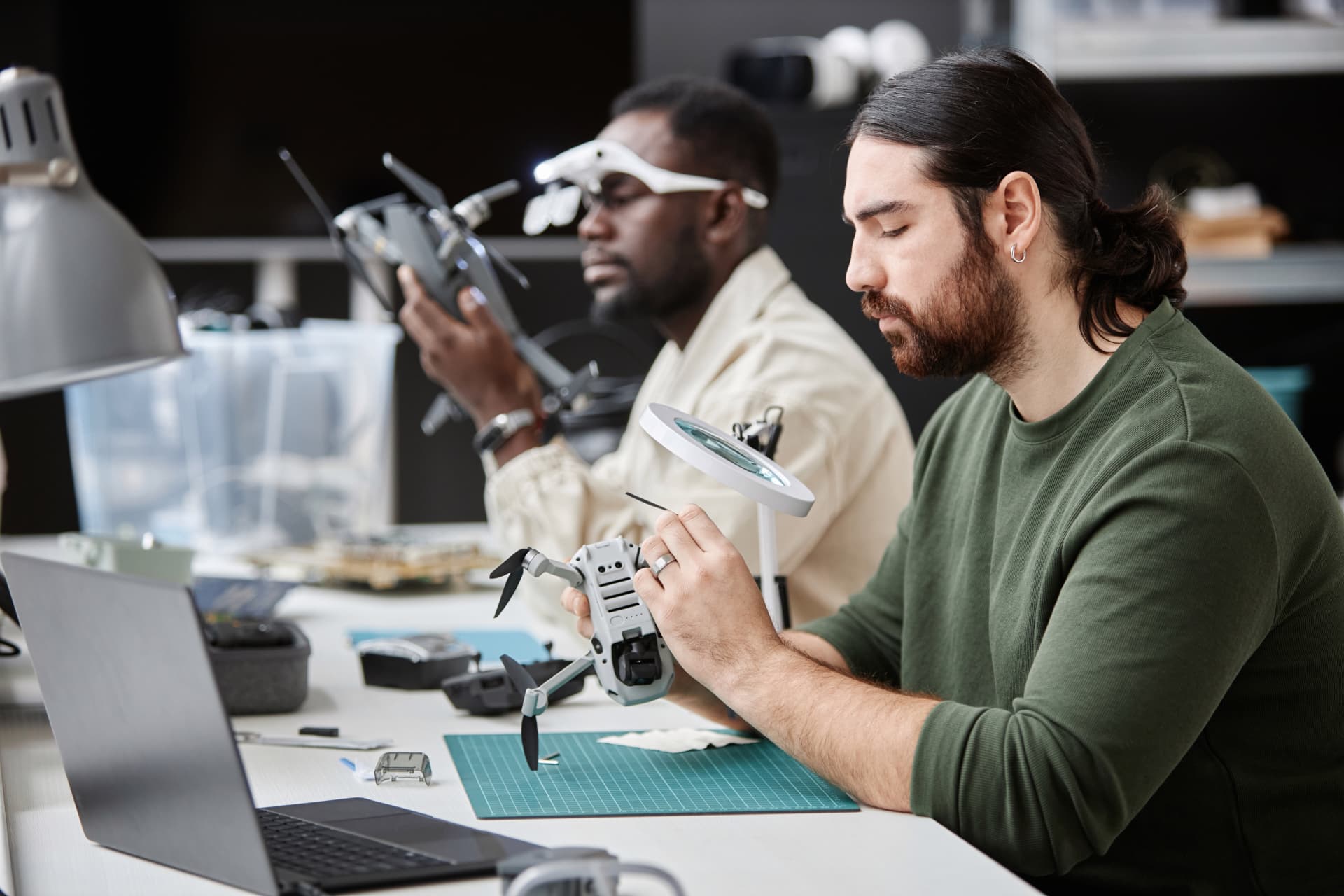 Engineers assembling hardware at a workshop bench with a laptop nearby